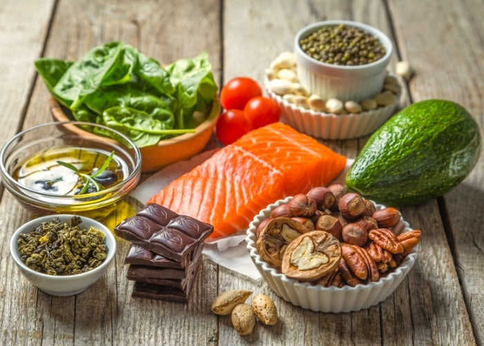 Schokolade, Öl, Spinat, Nüsse, Lachs, Saaten und Avocado als gesunde Ernährung auf einem Holztisch