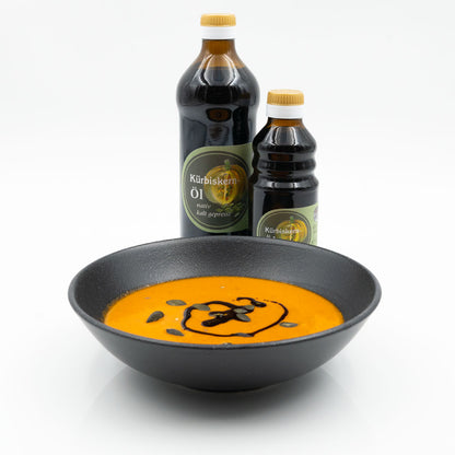 Kürbissuppe mit Kürbiskernöl und Kürbiskernen, dahinter zwei Flaschen Kürbiskernöl der Ölmühle Garting
