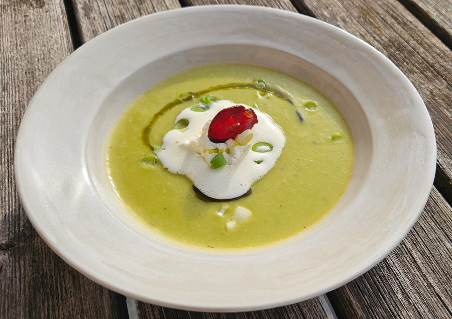 Grüne Lauchsuppe, garniert mit Frühlingszwiebel und Sahne in weißem Suppenteller auf Holztisch