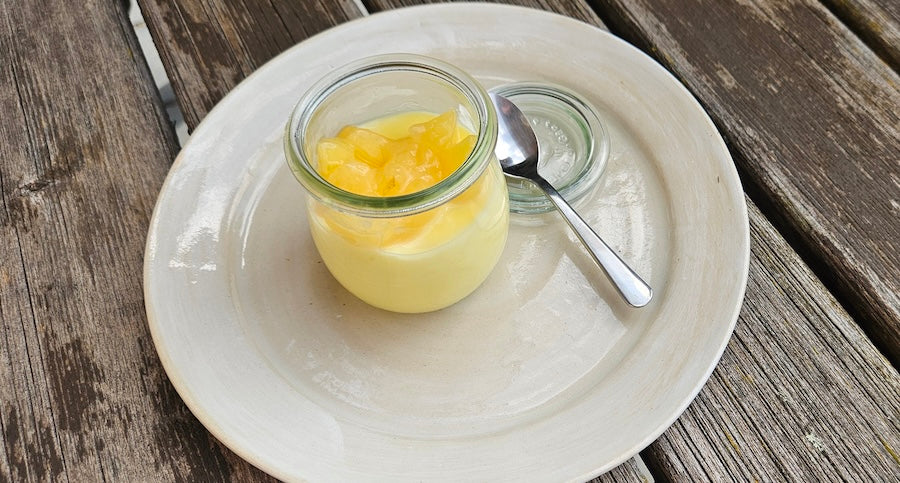 Pudding mit Kirschkernöl in einem Glas auf weißem Teller, im Hintergrund ein Holztisch