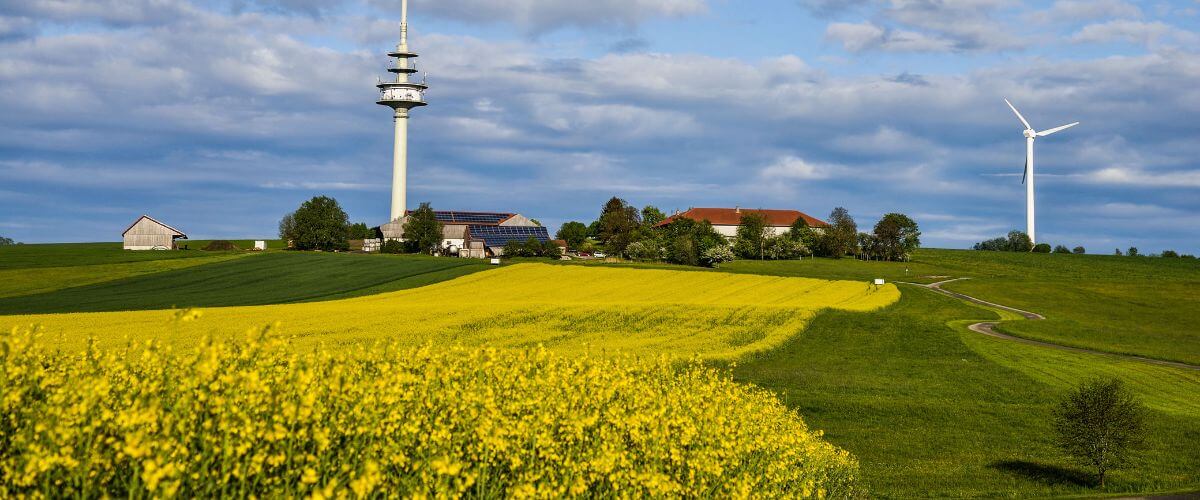 Ölmühle Garting und Fernsehturm Schnaitsee, im Vordergrund gelb blühendes Rapsfeld
